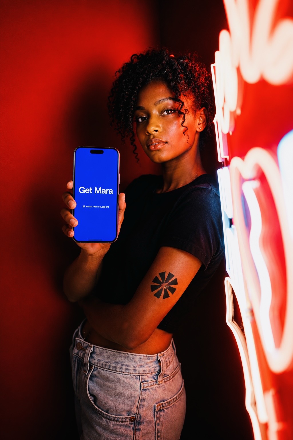 A woman holding a phone showing Mara, lit by red neon