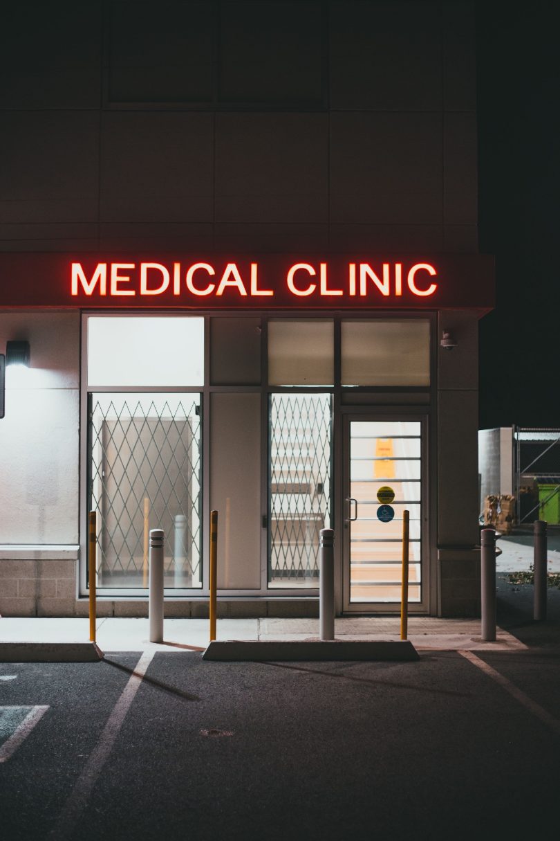 A medical clinic at night, its red neon sign lit above the door
