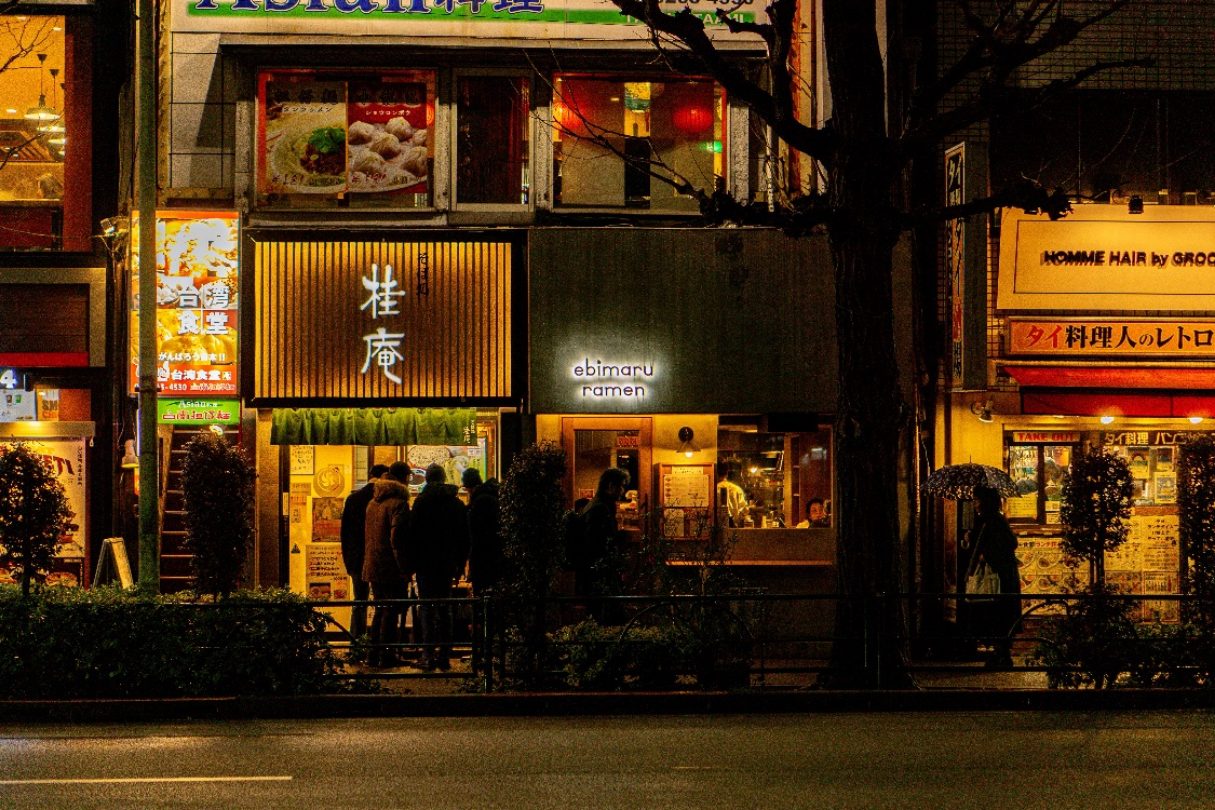 People queueing outside a lit ramen shop on a street at night