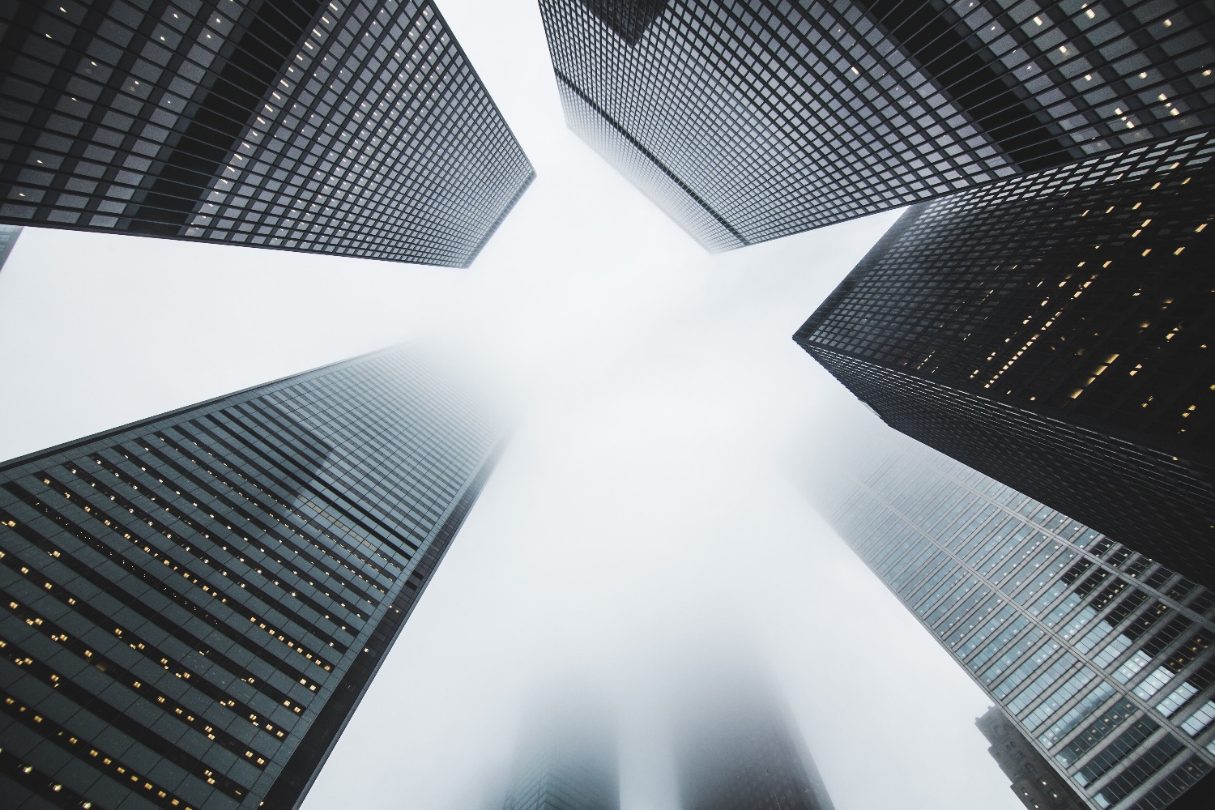 Office towers seen from the street below, disappearing into low cloud